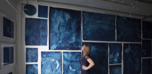 A photo of Desirée Patterson in front of a panel of artworks at Interglacial