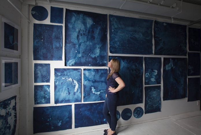 A photo of Desirée Patterson in front of a panel of artworks at Interglacial