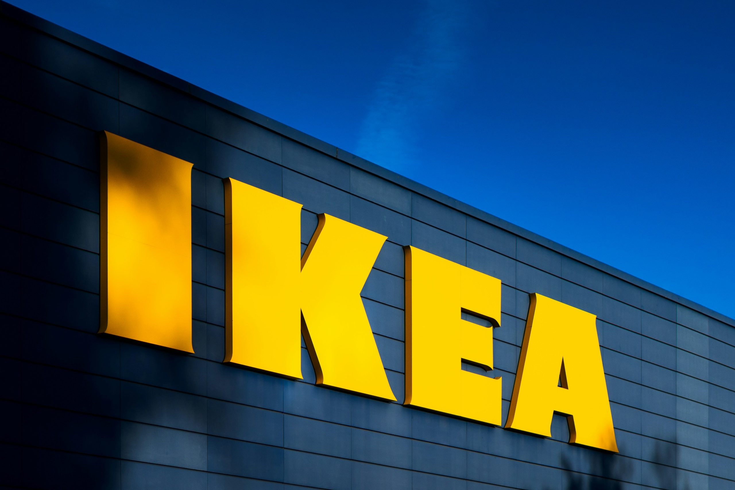 A photo of the yellow IKEA sign on a deep blue warehouse building.