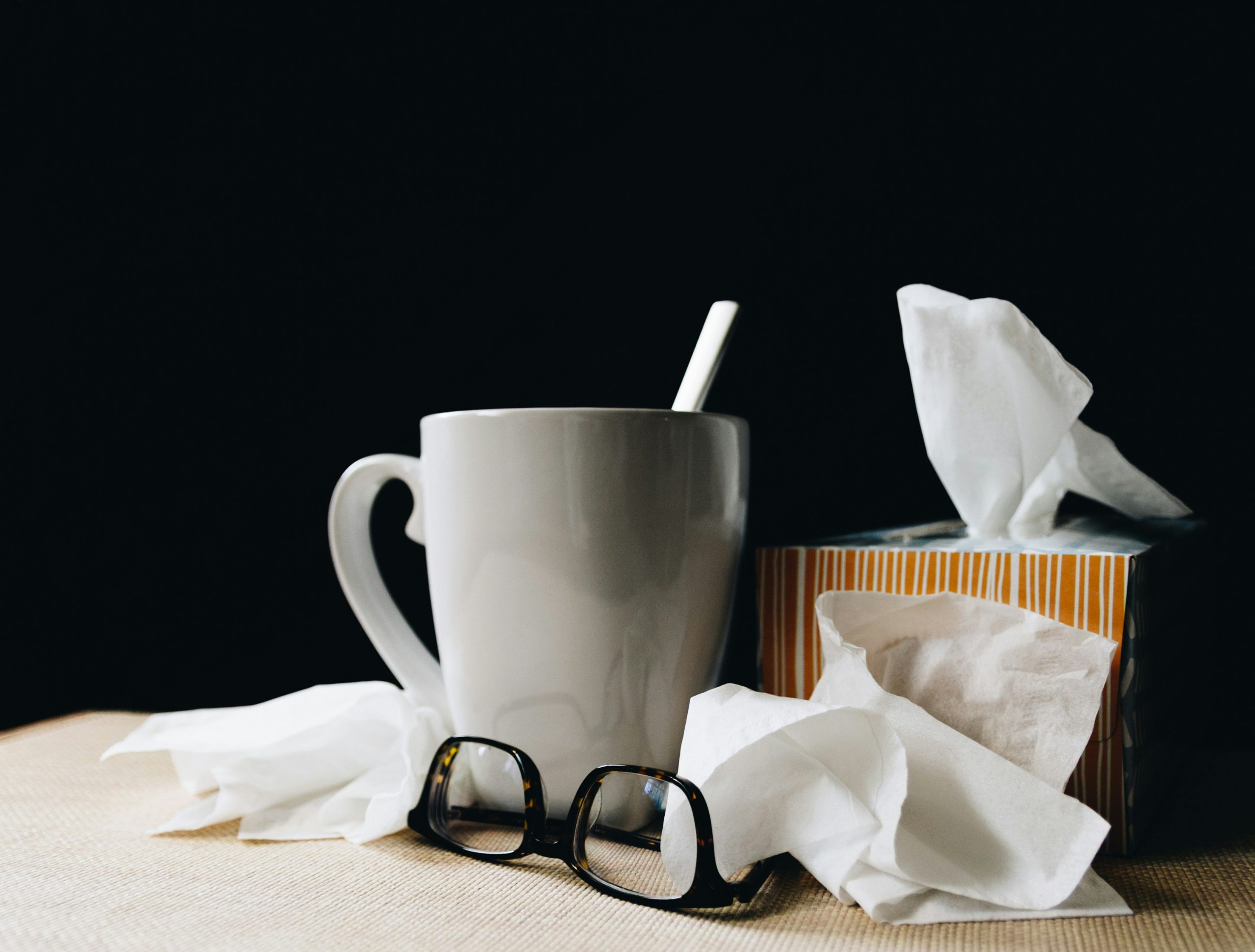 Coffee cup surrounded by glasses, a tissue box, and crumpled tissues