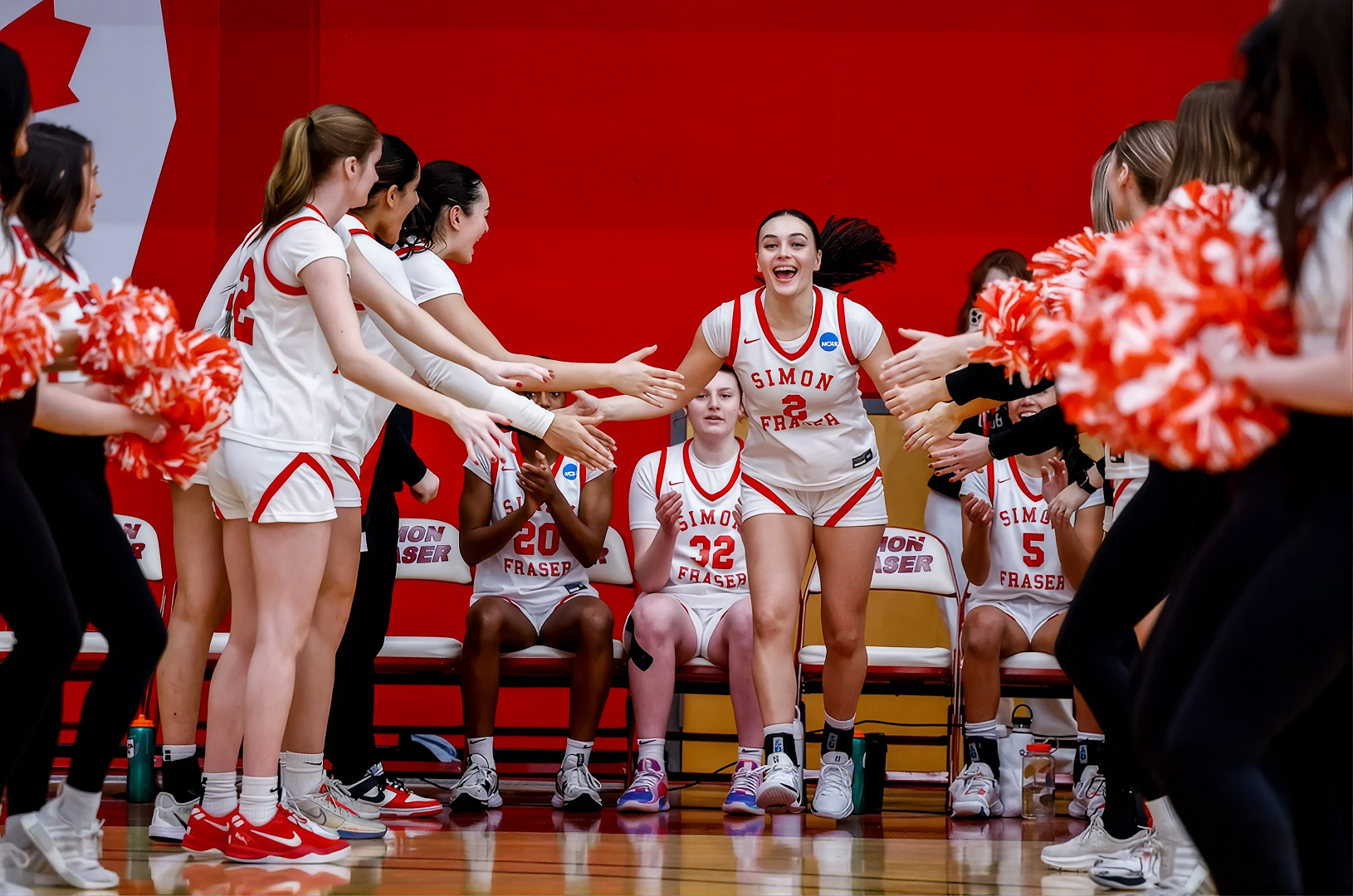 SFU female athlete high-fiving teammates and surrounded by cheerleaders in a gym