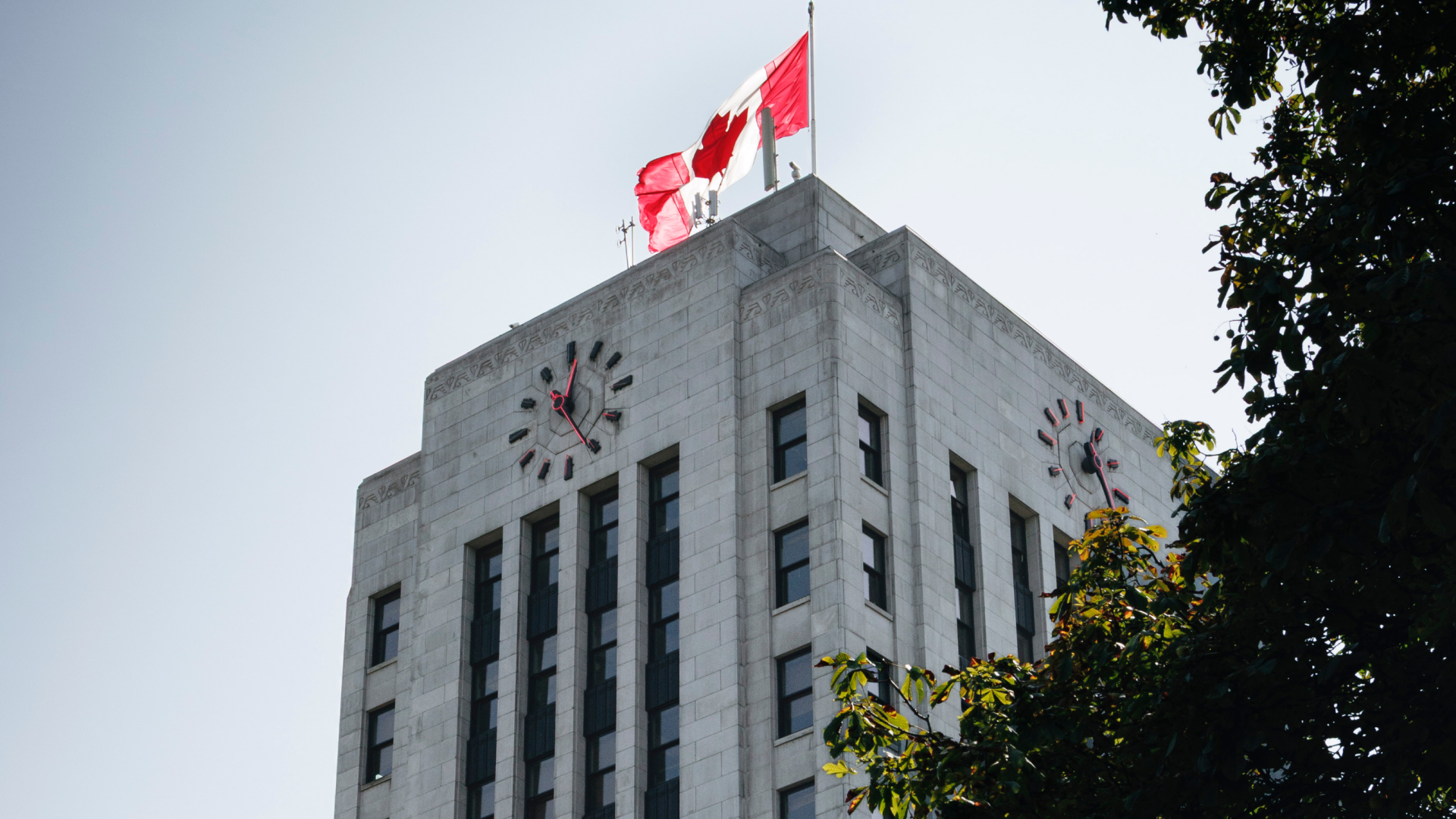 Vancouver city hall building featuring a clock and a Canadian flag